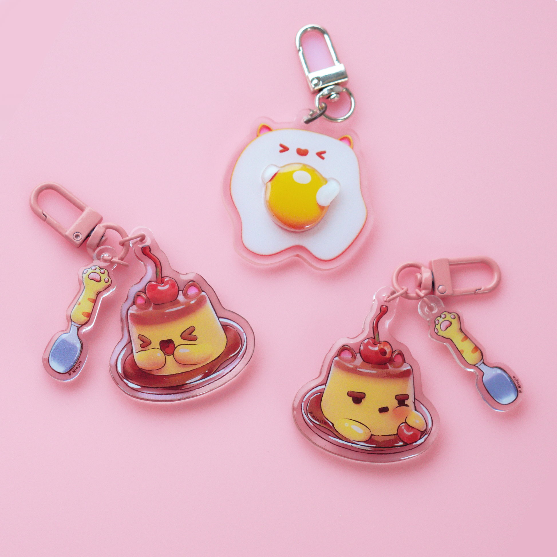 Egg keychain with >.< face and cute cat ears. The keychain has a 3D yolk. And Golden clamp. Displayed here with our McFlan keychains