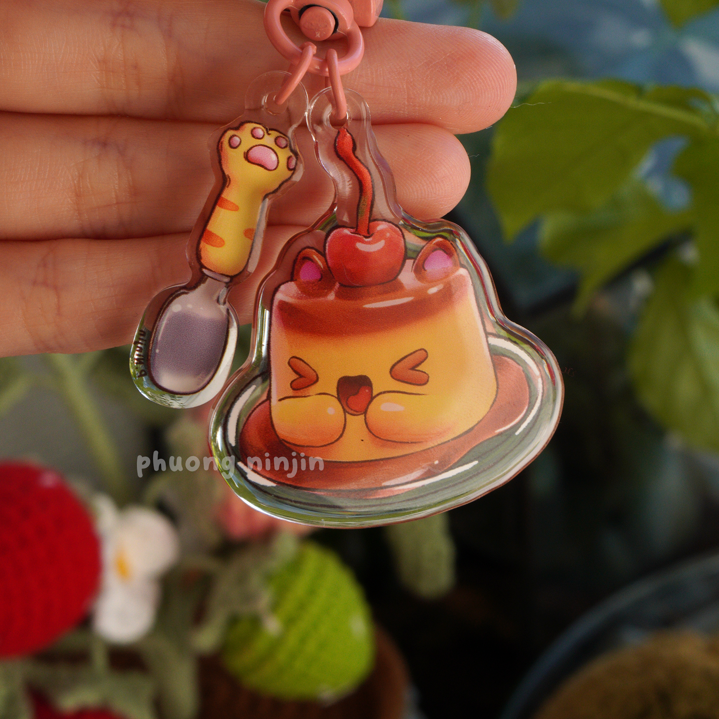 Dual sided flan keychain with cat ears and cherry on top. Along side a cat paw spoon. Displayed here is the happy flan face side
