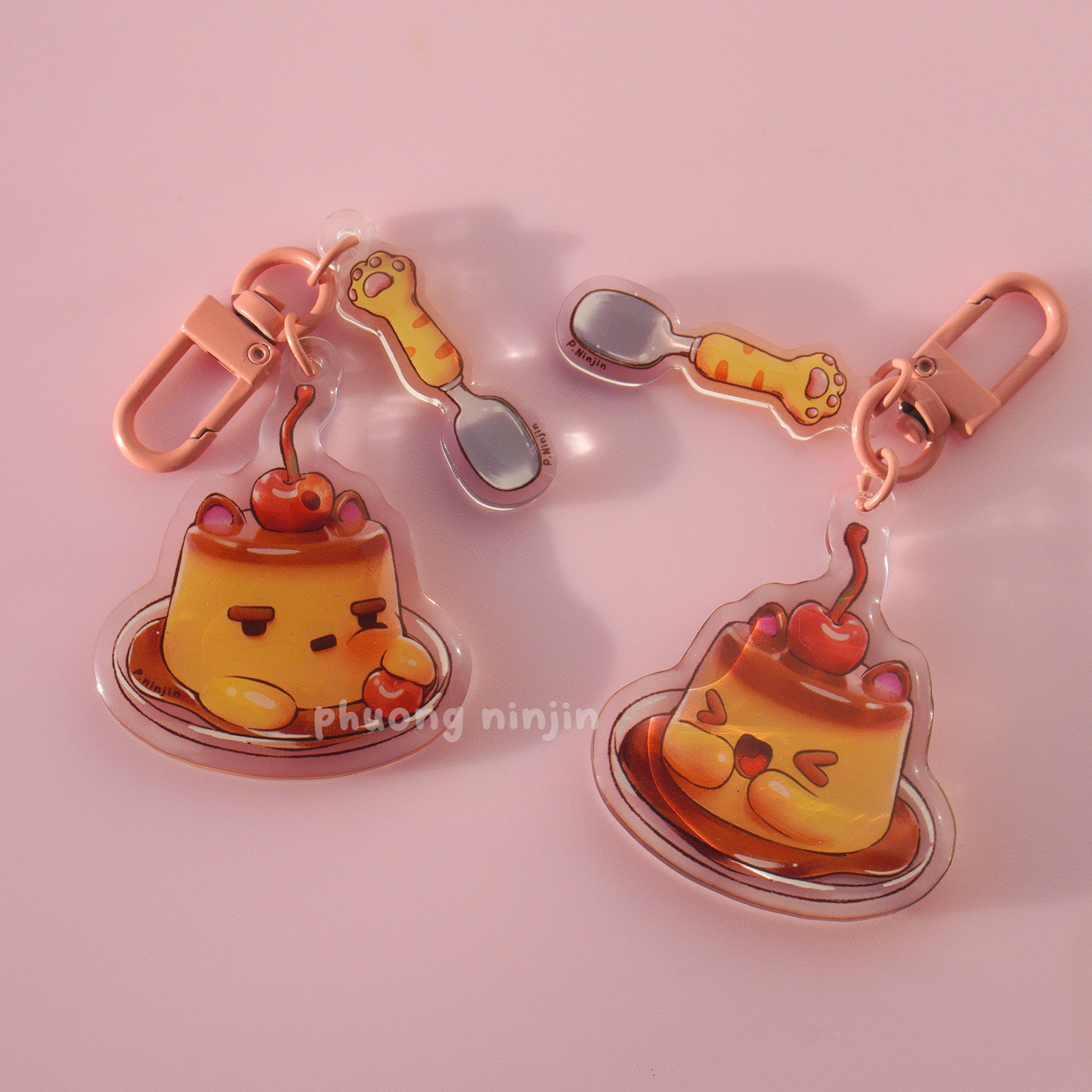 Dual sided flan keychain with cat ears and cherry on top. Along side a cat paw spoon. Both sides displayed here next to each other