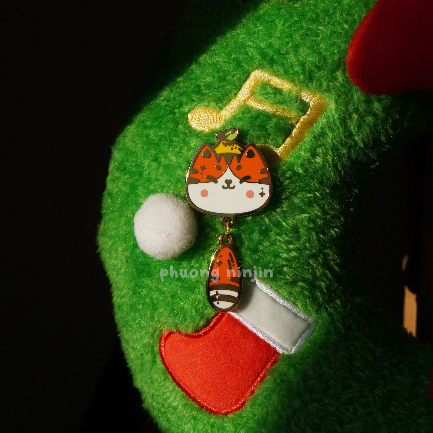 Yuzu cat with small lemon enamel pin with golden edges, displayed on some Christmas decoration.
