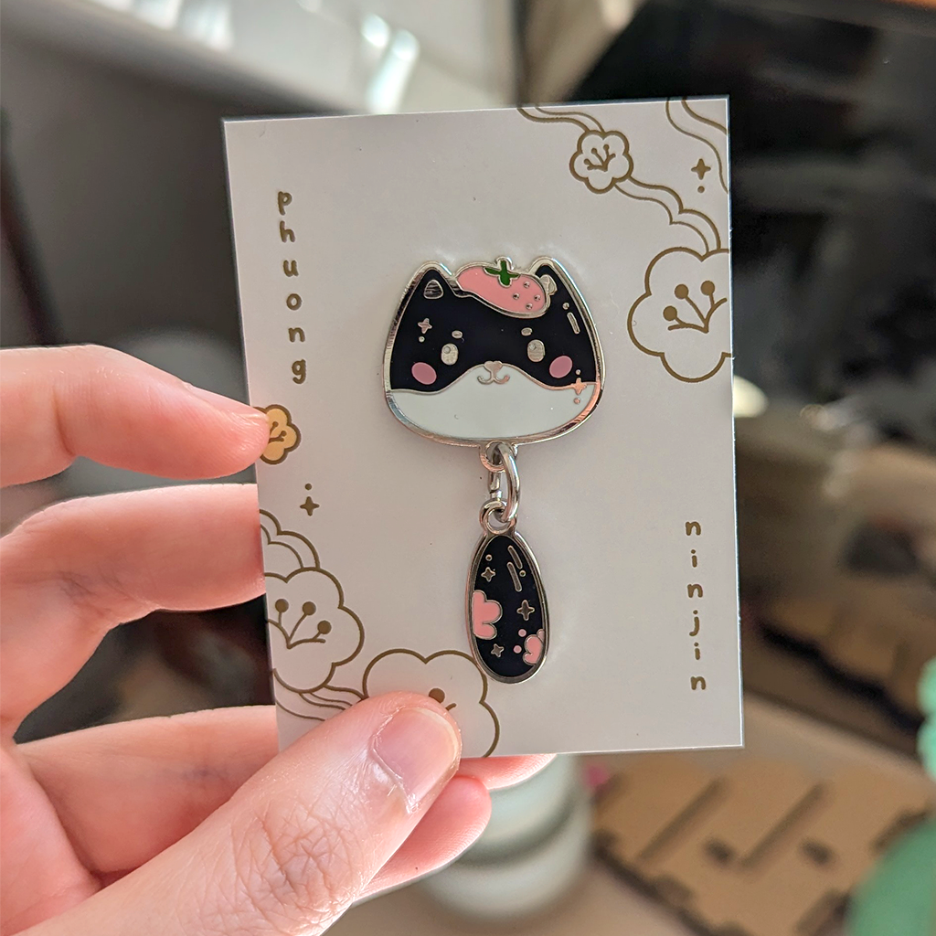 Mira cat enamel pin with silver edges displayed on our back card.