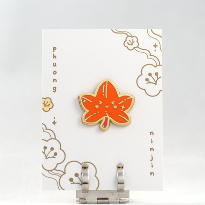 Maple leaf enamel pin with golden edges displayed here on our back card